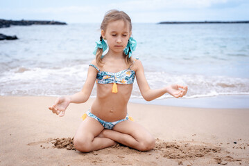 A little girl in a swimsuit runs on a sandy beach in Georgia and plays with the waves
