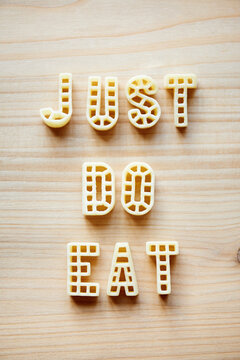 Naklejki Creative remade phrase ‘Just do eat’ made up of alphabet pasta against wooden table background 