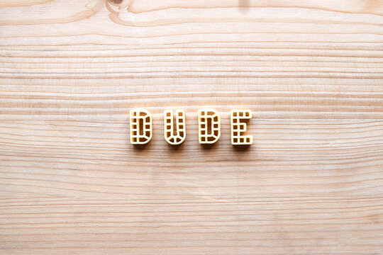 Conceptual photo of alphabet pasta forming a word &lsquo;dude&rsquo; against wooden table background 