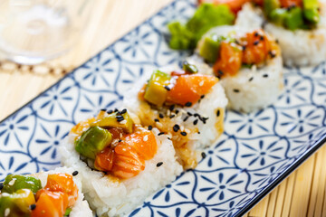 Plate of delicious sake maki rolls with salmon pieces, avocado, crab and cucumbers served with spicy wasabi, pickled ginger and soy sauce. Traditional Japanese snack