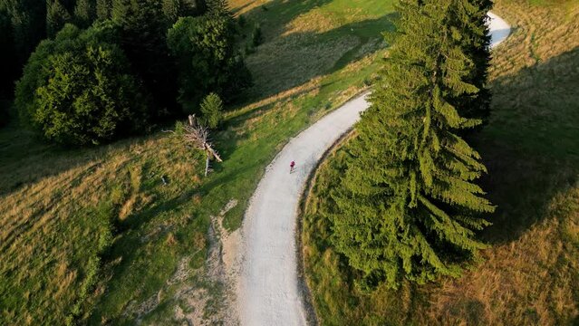 Top view drone footage of a female cyclist is riding on a gravel road between the mountains at sunset. Gravel cycling adventure.
