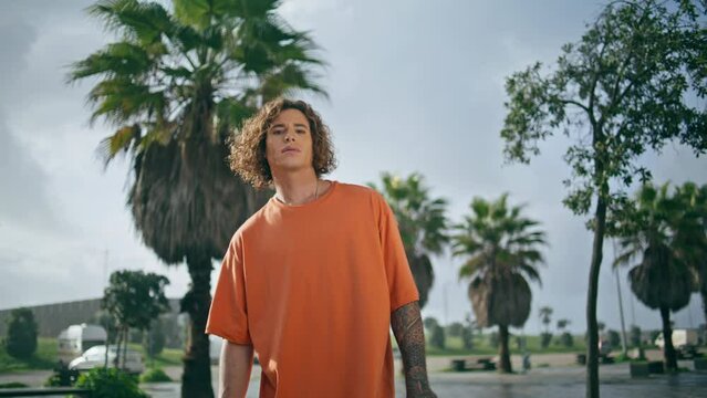 Young tattooed man posing street with tropical palms close up. Cool guy standing