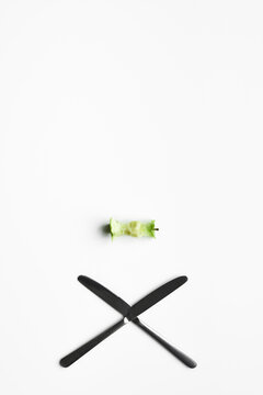 Conceptual shot of green apple core and crossed table knives isolated on white background 
