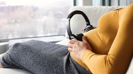 Pregnant woman holding headphones on belly listening to music for unborn baby brain development. Foetus can hear through the womb