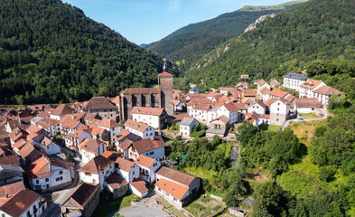 Scenic aerial view of spanish township of Isaba with brownish tiled roofs of residential buildings and medieval fortified church of Saint Cyprian in Roncal valley surrounded by green Pyrenees, Navarre © JackF