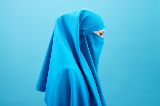 Profile portrait of mysterious woman in blue niqab against blue background  