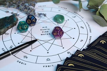 Zodiac wheel with sign triplicities, pen, tarot cards, gemstones and astrology dices on table,...