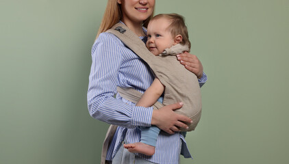 Mother holding her child in sling (baby carrier) on olive background, closeup