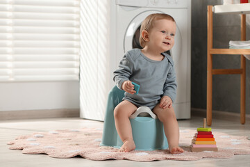 Little child sitting on plastic baby potty indoors. Space for text