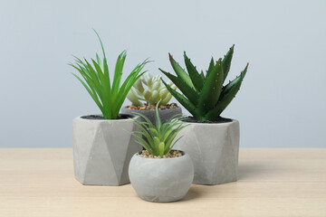 Many different artificial plants in flower pots on wooden table against light grey background