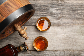Glasses and bottle of whiskey with wooden barrel on table, flat lay. Space for text