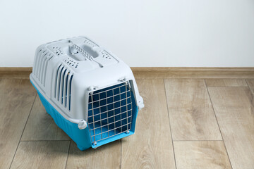 Light blue pet carrier on floor near white wall. Space for text