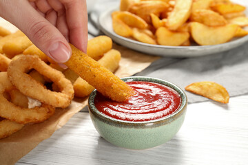 Woman dipping cheese stick into bowl with tasty ketchup at white table, closeup