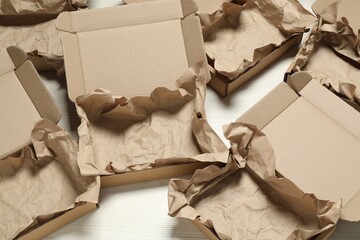Many open cardboard boxes with crumpled paper on white wooden floor, above view