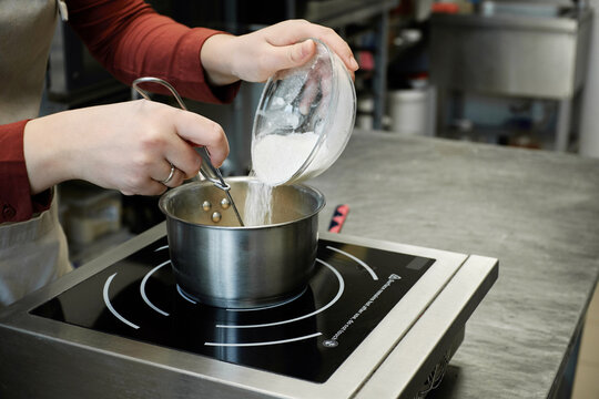 Unrecognizable female confectioner adding powdered sugar to fruit topping being cooked in saucepan in restaurant kitchen   