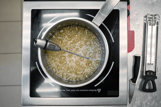 Directly above view of saucepan with sugar melting in boiling water and kitchen thermometer measuring temperature   