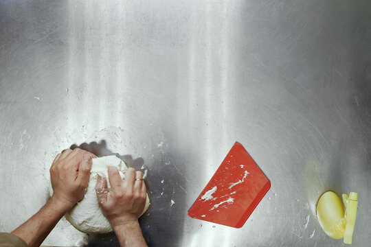 Directly above view of unrecognizable cook kneading dough on stainless steel  table in restaurant kitchen 