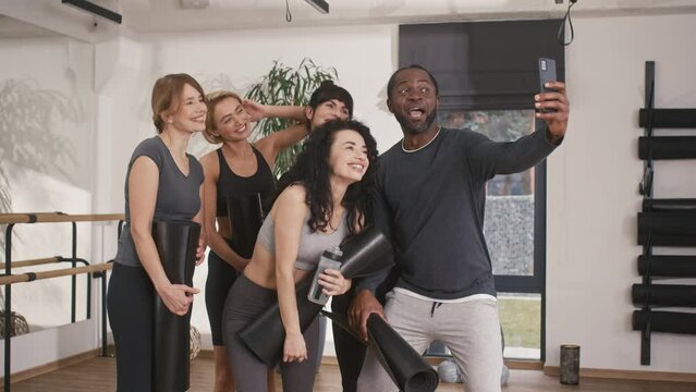 Multiethnic group of friends are completing their selfie photo. Making funny faces and joking. Smiling and showing positive emotions. Holding their yoga mats while posing for perfect shot.