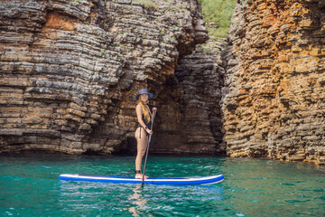 Young women Having Fun Stand Up Paddling in blue water seaamong the rocks in Montenegro. SUP