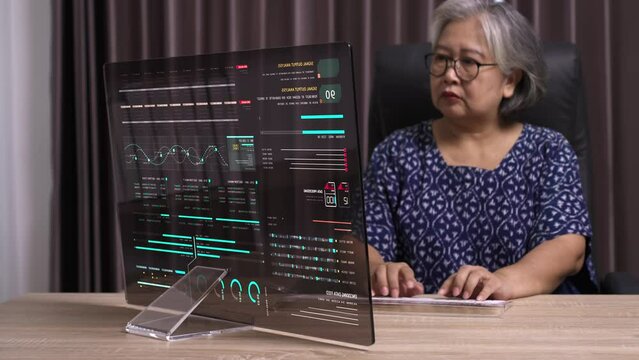 Senior woman typing on desktop computer with transparent monitor at workplace