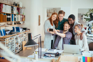 Young and diverse group of coworkers taking a selfie with a smart phone in the startup company office