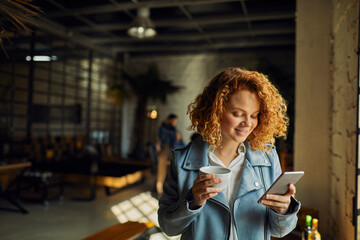 Young caucasian woman using a smart phone while having a coffee on her break while working in a startup company office