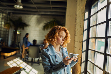 Young caucasian woman using a smart phone while having a coffee on her break while working in a startup company office