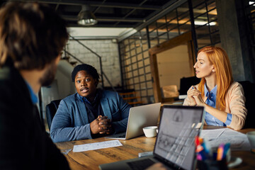 Young and diverse group of coworkers working on a project and having a meeting in a startup company...