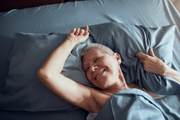 Senior woman with short hair waking up in the morning in her bed in the bedroom