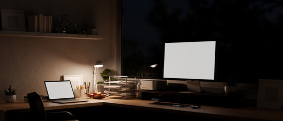 Modern office workspace at night with a computer and laptop on a table. Dark workspace