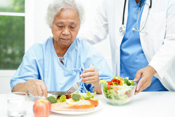 Asian elderly woman patient eating salmon stake and vegetable salad for healthy food in hospital.