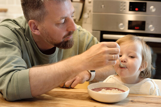 Infant girl eating with father help