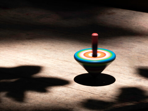colorful striped wooden top toy spinning on old wooden table under tree shadow.