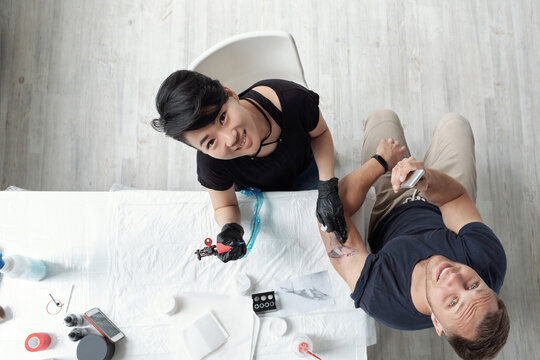 Smiling artist making tattoo and her client