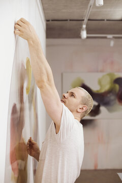 Man hanging artwork on wall in studio