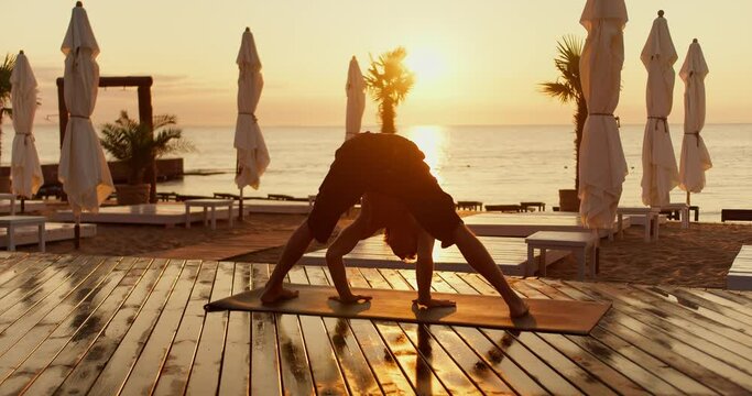 The guy gets on his head in a special yoga exercise on the beach in the morning. Yoga classes at dawn healthy lifestyle