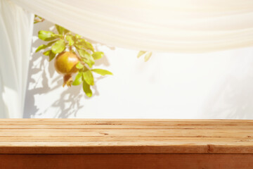 Jewish holiday Sukkot concept. Empty wooden table over pomegranate tree and sukkot background....