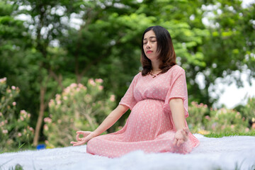 Portrait of asian pregnant woman relaxing by meditating in park