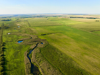 Small river flows among fields illuminated by sunset light