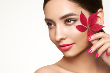 Fototapeta premium Portrait of beautiful young woman with autumn leafs. Healthy clean fresh skin natural make up beauty eyes and red nails