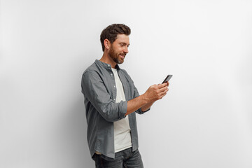 Smiling man looking to his mobile phone while standing on white background