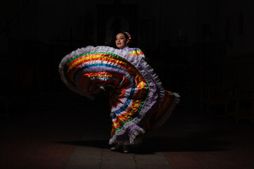 Latina woman dressed as a Chinese problem with a skirt bordered with colorful sequences, a red cloak, braided bows and a smiling black background.