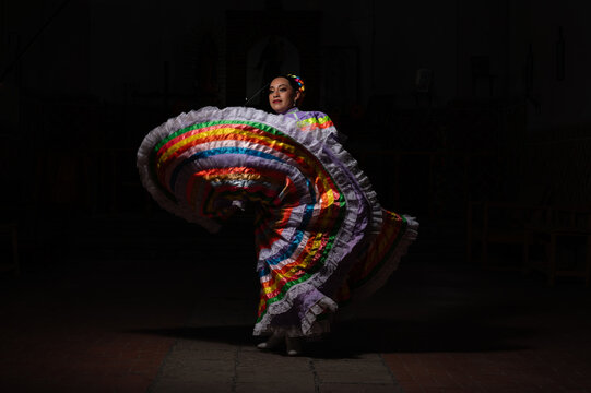 Latina woman dressed as a Chinese problem with a skirt bordered with colorful sequences, a red cloak, braided bows and a smiling black background.