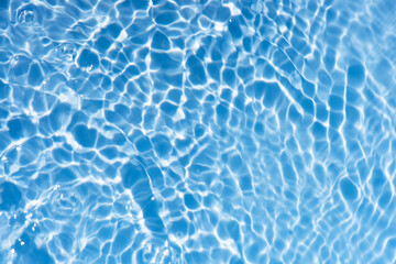 Blue water with ripples on the surface. Defocus blurred transparent blue colored clear calm water surface texture with splashes and bubbles. Water waves with shining pattern texture background.