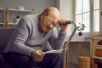 Emotional pensioner. Depressed disappointed elderly man reading bad news from paper document or...
