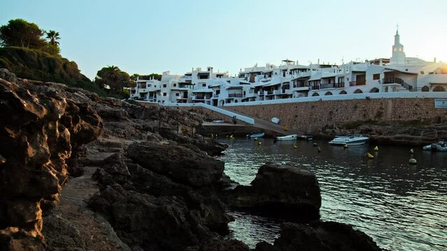 Beautiful rocky seashore with Binibeca Vell in the background in Menorca, Spain. A view of a Spanish resort with hotels and relaxing nature on the Balearic Islands.