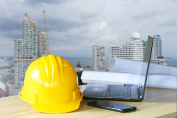 Yellow engineer hat on the table There is a laptop and construction plans. ,under the concept of construction and design