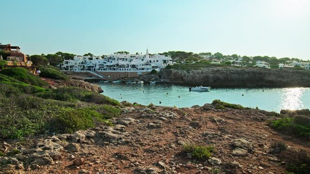Beautiful rocky seashore with Binibeca Vell in the background in Menorca, Spain. A view of a Spanish resort with hotels and relaxing nature on the Balearic Islands.