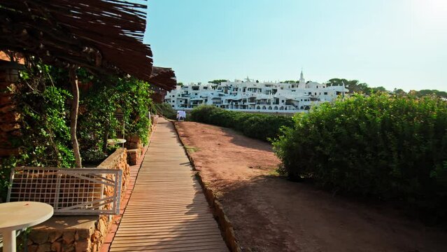Beautiful sunrise over a seashore in Menorca with a wooden sidewalk and nature. Walking on a footpath pavement made of wood by the sea in Binibeca Vell, Balearic Islands, Spain.