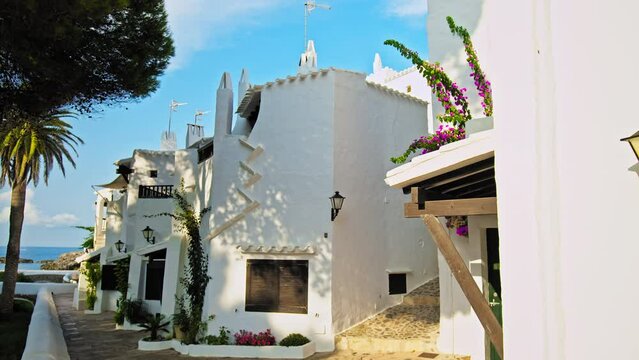 Scenic view of Binibeca Village with whitewashed houses and tropical green trees. Relaxing tourist resort Binibeca Vell with narrow streets and a calm cove - paradise-like town in Menorca, Spain.